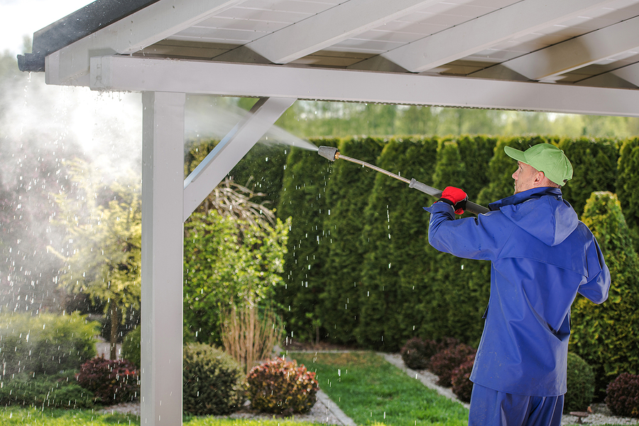 men in his 30s pressure washing garden porch wooden roof which get dirty during winter season