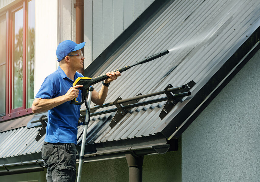 man standing on ladder and cleaning house metal roof with high pressure washer